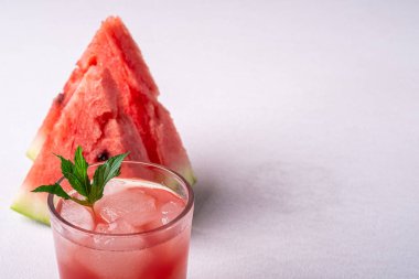 Beyaz arka planda iki dilim karpuz, fotokopi alanı, açı görünümü, seçici odak cam içecek buz küpleri ve yeşil nane yaprağı ile taze soğuk karpuz suyu