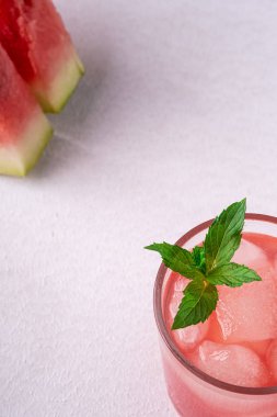 Beyaz arka planda iki dilim karpuz, fotokopi alanı, açı görünümü, seçici odak cam içecek buz küpleri ve yeşil nane yaprağı ile taze soğuk karpuz suyu