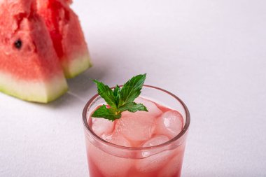 Beyaz arka planda iki dilim karpuz, fotokopi alanı, açı görünümü, seçici odak cam içecek buz küpleri ve yeşil nane yaprağı ile taze soğuk karpuz suyu