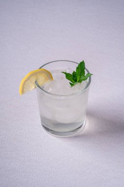 Beyaz gri arka plan üzerinde buz küpleri, limon dilimi ve nane yaprağı ile cam taze soğuk berrak su içeceği