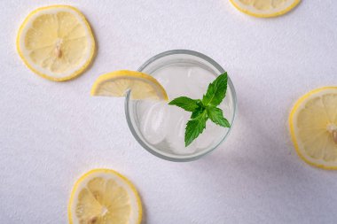 Buz küpleri ile cam taze soğuk berrak su içeceği, limon dilimi ve nane yaprağı limon dilimleri yakın, beyaz gri arka plan, üst görünüm, düz yatıyordu