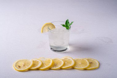 Buz küpleri, limon dilimi ve nane yaprağı limon dilimleri yakın, beyaz gri arka plan, açı görünümü, seçici odak ile cam taze soğuk berrak su içeceği