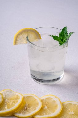 Buz küpleri, limon dilimi ve nane yaprağı limon dilimleri yakın, beyaz gri arka plan, açı görünümü, seçici odak ile cam taze soğuk berrak su içeceği