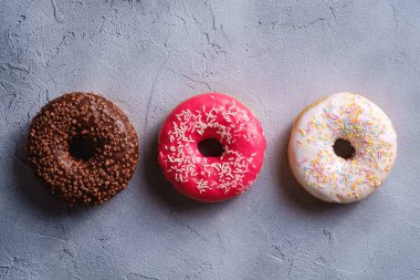 Arka arkaya üç çörek, çikolata, pembe ve vanilyalı çörek, üzerine şeker serpiştirilmiş tatlı yiyecekler beton desenli arka plan, üst manzara