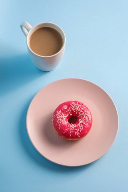 Kahve fincanının yanına serpiştirilmiş pembe çörek, tatlı jöleli tatlı yiyecekler ve mavi arka planda sıcak içecek, açı manzaralı.