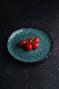 Çeri domates dalı, taze olgun organik sebzeler koyu siyah desenli arka planda mavi yeşil plaka, açı görünümü kopyalama alanı