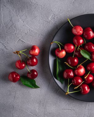 Siyah tabakta yeşil yapraklı taze kiraz meyveleri. Gri taştan arka planda yaz vitamini meyveleri.