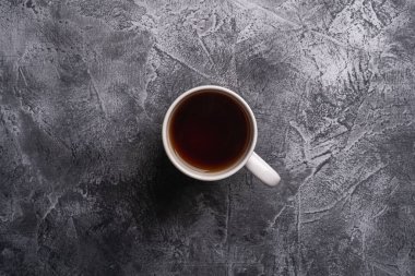 Bir seramik fincan, sıcak siyah çay, beyaz çay fincanı, desenli koyu taş arka plan, üst manzara.