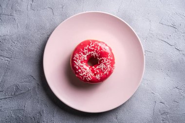 Pembe tabağa serpiştirilmiş pembe çörek, beton desenli arka planda tatlı jöleli tatlı yiyecekler, üst manzara.