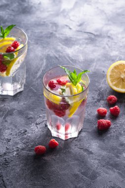 Limonlu, ahududu meyveli ve naneli taze soğuk su içeceği. Taş beton zemin üzerinde iki yüzlü bardak, yaz diyet içeceği, seçici bakış açısı.