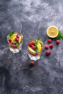 Limonlu, ahududu meyveli ve naneli taze soğuk su içeceği. Taş beton zemin üzerinde iki yüzlü bardak, yaz diyet içeceği, seçici bakış açısı.