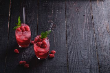 Nane şekerli taze buzlu meyve suyu, iki bardakta ahududu limonatası, koyu ahşap arka planda pipetler, açı görüşlü kopyalama alanı.