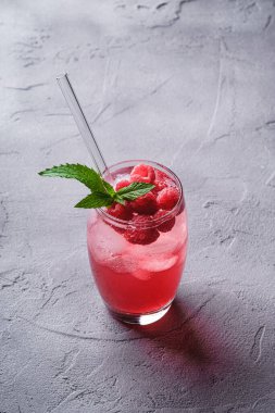 Naneli taze buz gibi meyve suyu, bardakta ahududu limonatası taş betondan arka planda pipetler, açı manzaralı.