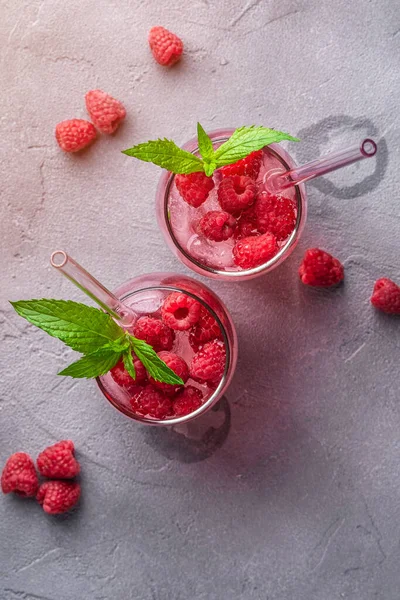 Fresh ice cold berry juice drink with mint, summer raspberry lemonade in two glass with straws on stone concrete background, top view