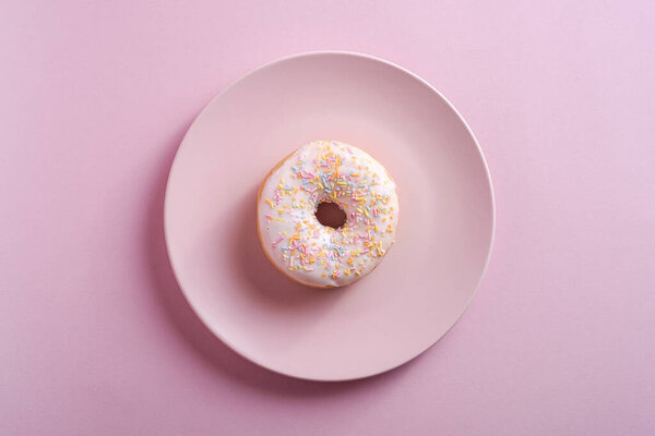 Vanilla donut with sprinkles on pink plate, sweet glazed dessert food on pink minimal background, top view