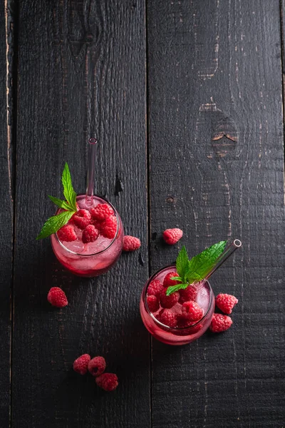 Fresh ice cold berry juice drink with mint, summer raspberry lemonade in two glass with straws on dark wooden background, top view copy space