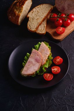 Hindi jambonlu sandviç, yeşil salata ve siyah tabakta taze vişneli domates dilimleri kesme tahtasındaki malzemelerin yanında, koyu dokulu arka plan, açı görüşlü.