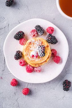Süzme peynir krepleri ve pudra şekeri, kremalı börek, ahududu ve böğürtlenli tatlı tabakta, taş zeminde limon dilimli sıcak çay fincanının yanında, üst manzara