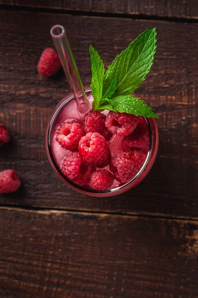 Fresh ice cold berry juice drink with mint, summer raspberry lemonade in glass with straws on brown wooden background, top view macro