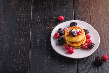 Süzme peynirli krep ve pudra şekeri, kremalı börek, ahududu ve böğürtlenli tatlı koyu siyah ahşap arka planda, açılı kopya alanı