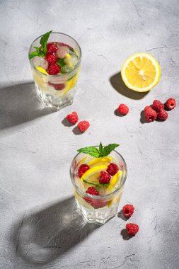 Limonlu, ahududu meyveli ve naneli taze soğuk su içeceği. Taş zeminde iki yüzlü bardak, yaz diyet içeceği, açı görüşlü.
