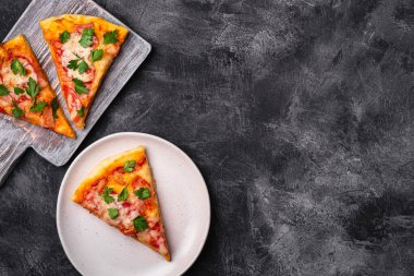 Sıcak pizza dilimleri mozzarella peyniri, jambon, domates ve maydanoz ahşap kesim tahtası ve tabak, taş beton arka plan, metin için üst görünüm kopyalama alanı