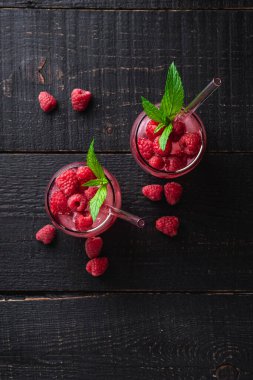 Nane şekerli taze buzlu meyve suyu, iki bardakta ahududu limonatası, koyu ahşap arka planda pipetler, üst manzara.