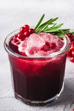 Bardakta taze buz gibi meyve kokteyli, ferahlatıcı kırmızı frenk üzümü içeceği, taş zeminde biberiye yaprağı, açı açılı makro.