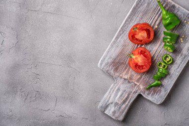 Eski ahşap kesim tahtasının üzerinde acı biberli taze domates dilimlenmiş taze domates, taş beton arka plan, üst görünüm kopya alanı