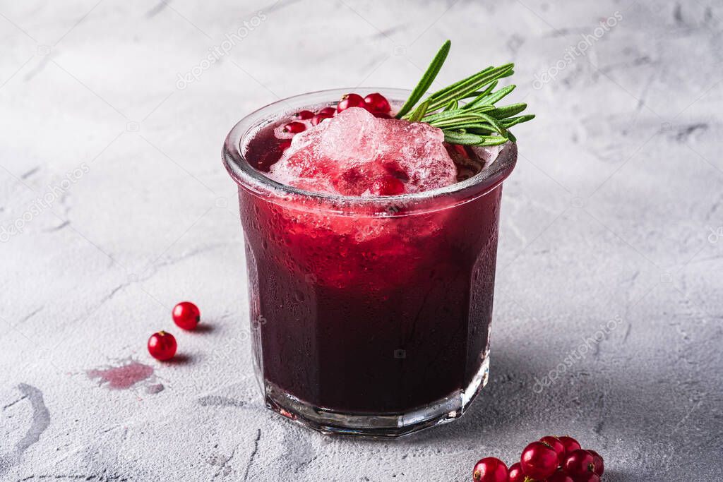 Fresh ice cold fruit cocktail in glass, refreshing summer red currant berry drink with rosemary leaf on stone concrete background, angle view
