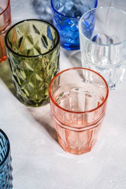 Renkli ve geometrik içecek kadehleri, boş yeşil, kırmızı, mavi ve şeffaf içecek takımları taş beton arka plan, açı görünümü