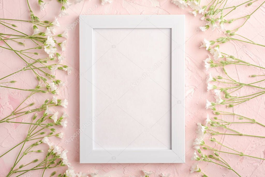 White empty photo frame mockup with mouse-ear chickweed flowers on pink textured background, top view copy space