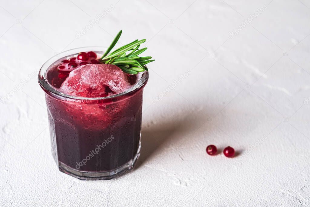 Fresh ice cold fruit cocktail in glass, refreshing summer red currant berry drink with rosemary leaf on white background, angle view