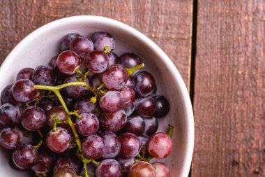 Kahverengi ahşap arka planda taze üzümlü meyve kasesi.