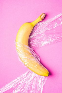 Muz meyvesi, pembe zemin üzerine plastik sarılı, minimalist yaratıcı düzen, ekoloji ve çevre kavramı