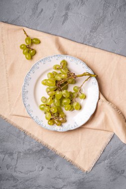 Taze beyaz üzüm üzümleri tabakta keten masa örtüsü, taş beton arka plan, üst manzara.