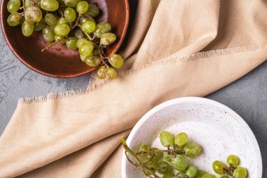 Taze beyaz üzüm üzümleri iki ahşap kasede keten masa örtüsü, taş beton arka plan, üst manzara.
