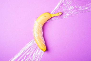 Muz meyvesi, pembe zemin üzerine plastik sarılı, minimalist yaratıcı düzen, ekoloji ve çevre kavramı