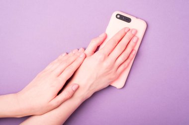 Güzel kadın elleri taze manikür yapıyor ve elinde akıllı telefon, deri ve tırnak bakımı konsepti, mor arka plan.