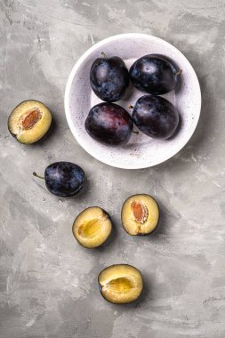 Taze olgun erik meyveleri, ahşap bir kasede dilimlenmiş taş beton arka plan, üst manzara.