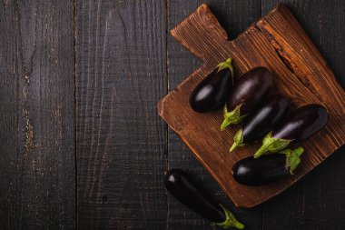 Kahverengi ahşap kesme tahtasındaki taze patlıcan, koyu ahşap arka plan, üst görünüm kopyalama alanı