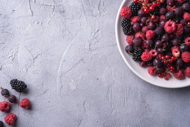 Lezzetli taze ahududu, böğürtlen, bektaşi üzümü ve üzümlü üzümler tabakta, beton zeminde sağlıklı besin meyvesi, üst görünüm kopya alanı