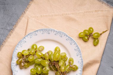 Taze beyaz üzüm üzümleri tabakta keten masa örtüsü, taş beton arka plan, üst manzara.