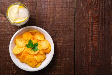 Limonlu taze soğuk su içeceği patates cipsinin yanında maydanoz yaprağı ahşap arka planda ahşap kasede, en üstte fotokopi alanı