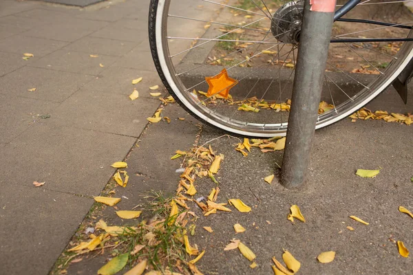 Kaldırımda sarı sonbahar yaprakları serpiştirilmiş, üzerinde turuncu yıldız yansıtıcısı olan park halindeki bisiklet tekerleğinin ayrıntıları