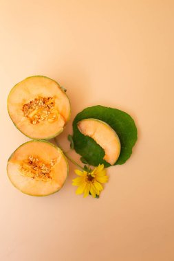 İki yarım kavun, görünür tohumlar, yeşil yaprakta bir dilim ve bej arka planda sarı bir ayçiçeği..