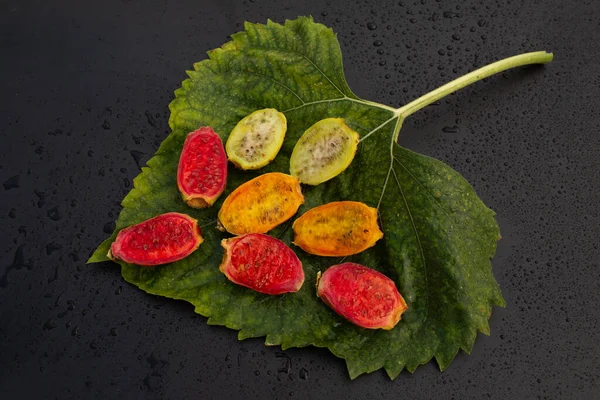 Bir yaprağın üzerinde kırmızı, turuncu ve yeşil posaları ortaya çıkarmak için kesilen çeşitli kaktüs armutları..