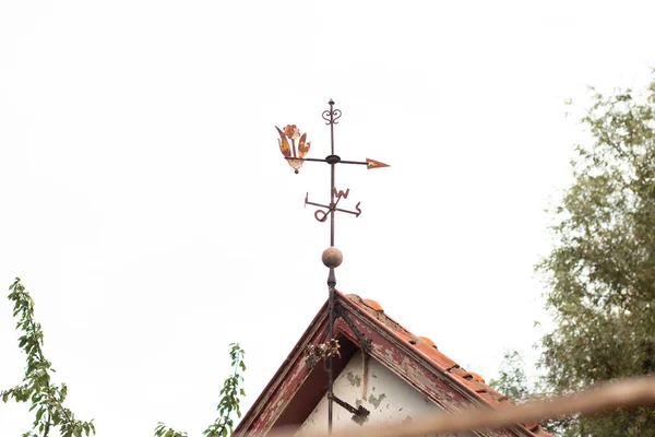 Eski bir çatının tepesinde ok ve dekoratif unsurla eski paslı rüzgar gülü.