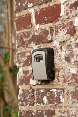 Detailed view of a grey lockbox with numeric code fixed on rustic red bricks.