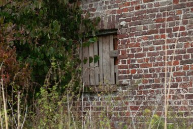 Yıpranmış ahşap bir pencere, terk edilmiş tuğla bir binanın kenarına tahta çakılmış..